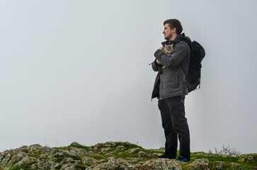 Young man with dark hair holds cat, standing on rocky crimean cliff. Gray sky creates serene,...