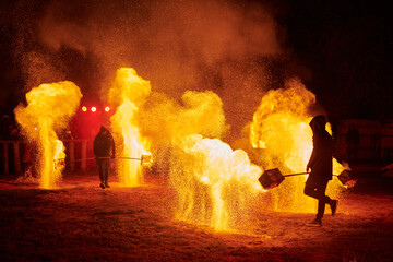 Silhouette of two fire performers with sparkling fire staff erupting in night sky, showcasing...