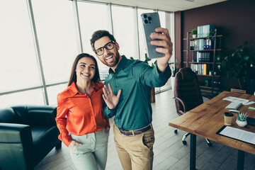 Obraz premium Two smiling coworkers in a modern office taking a selfie, showcasing teamwork and a collaborative corporate environment.