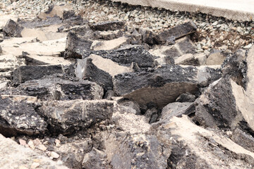 Asphalt broken into large pieces on the road. Repair work in the city. Road repair work. A mountain of removed asphalt pavement. Repair concept. A pile of asphalt debris close-up