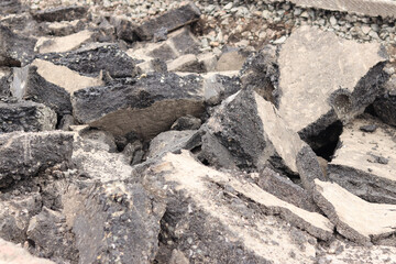 Asphalt broken into large pieces on the road. Repair work in the city. Road repair work. A mountain of removed asphalt pavement. Repair concept. A pile of asphalt debris close-up