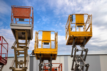 shot of several industrial scissor lifts with colorful platforms against a cloudy sky.