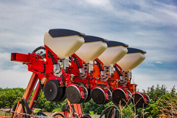 a modern red and white farm planter or seeder against a cloudy sky, ready for planting