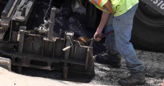 A slow motion close up view of workers on a paver machine on a city street.  	
