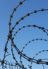 A close-up shot of razor wire fencing against a bright, clear, blue sky for security.