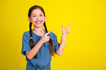 Charming young girl with braided hairstyle pointing happily on bright yellow background with...