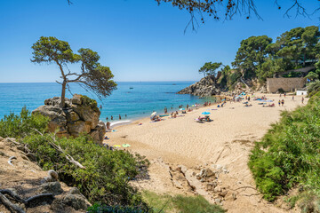 Tourists relaxing on sandy beach at picturesque cala cap roig in costa brava, spain