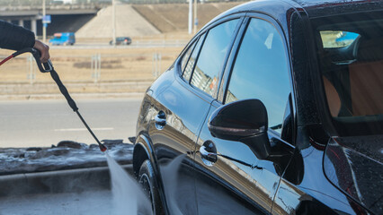 A self-service car wash featuring a high-pressure water spray cleaning a vehicle. Active foam covers the car's surface, effectively lifting dirt and grime for a thorough wash.