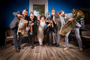 Jazz group dressed in retro costumes, crouching down and looking at the camera as a group, while pointing their instruments forward.