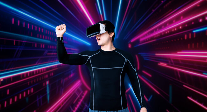 Smart male gamer with VR glasses celebrating for winning the game with glowing neon light. Excited player celebrate for victory in game while using augmented reality technology innovation. Ingenuity.
