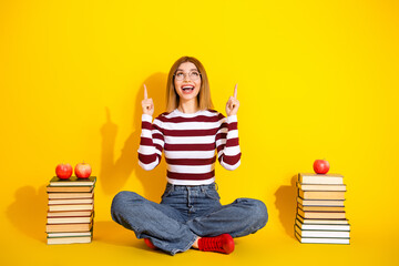 Young woman sitting with book on yellow background showing upward hand gestures, education and...