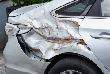 Damaged car rear side with severe dents and rust, showing aftermath of a collision or accident.
