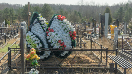 Artificial flowers and a lit candle lamp on a cemetery grave symbolize memory, faith, and hope for...