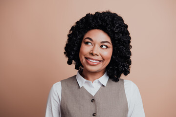 Portrait of a cheerful young businesswoman with curly hair in formal attire on a beige background