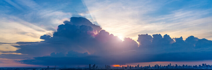 Vibrant sunset colors spread across the sky over a sprawling cityscape. Thick clouds create a...