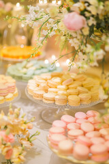 Delicate macarons in pastel hues arranged on tiered glass stands, surrounded by floral arrangements creating a festive confectionery display.