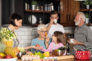 Three-generation family are joking with vegetables in kitchen