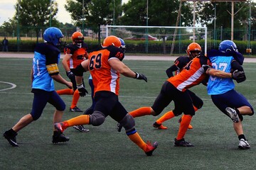 American football players in orange and black uniforms catch a player in blue and black uniforms on a green field	

