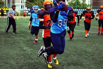A player in a blue and black uniform makes a jumping catch during an American football game.	
