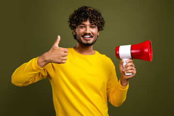 Smiling young man posing confidently with a megaphone in hand and giving a thumbs up against a...