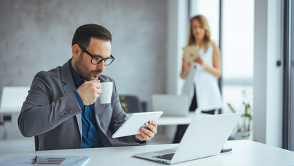 Businessman at Desk Using Tablet While Drinking Coffee in a Modern Office