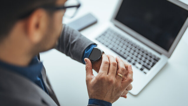 Businessman Checking Smartwatch While Using Laptop in Office Workspace
