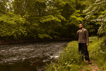 Caucasian man wearing a backpack walking in a forest next to a river watching the nature outdoors.