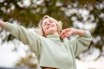 Joyful mature Easter European woman dancing with arms open in nature