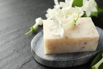 Bar of soap and jasmine flowers on black table, closeup. Space for text