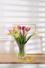 Bouquet of beautiful tulips and frames on wooden table indoors. Space for text