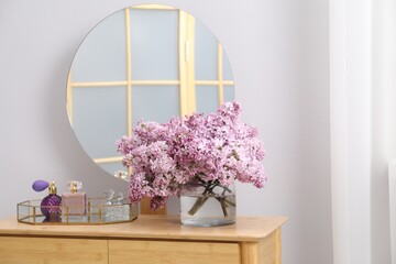 Beautiful lilac flowers in glass vase and perfumes on wooden table indoors