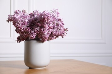 Beautiful lilac flowers in vase on wooden table near white wall indoors, space for text