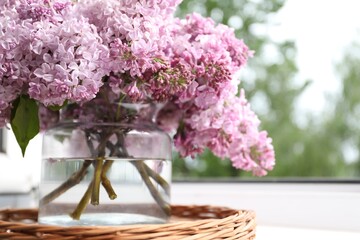 Beautiful lilac flowers in glass vase on window sill indoors, closeup. Space for text