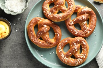 Tasty pretzels with salt and sauce on grey table, flat lay