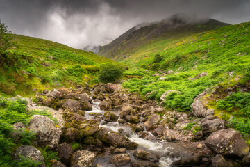 A serene stream winds through lush greenery, framed by majestic hills and soft clouds, creating a peaceful scene that brings joy and tranquility to observers, Kerry, Ireland