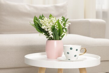 Bouquet of beautiful lily-of-the-valley and cup on coffee table indoors