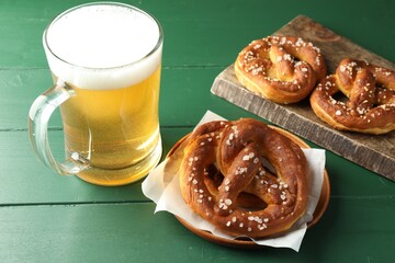 Tasty pretzels and glass of beer on green wooden table, closeup