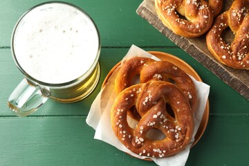 Tasty pretzels and glass of beer on green wooden table, flat lay