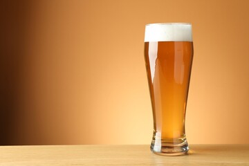 Fresh beer in glass on wooden table against beige gradient background, closeup. Space for text