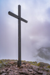 A towering cross stands majestically on top of Carrauntoohil mountain, shrouded in thick mist, representing both faith and serenity against a breathtaking mountain backdrop, Kerry, Ireland
