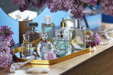 Bottles with perfumes, lilac flowers and accessories on dressing table indoors