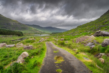 A picturesque path winds through a vibrant landscape, framed by majestic mountains and Black Valley, with dramatic sky an ideal spot for nature lovers and photographers, Kerry, Ireland