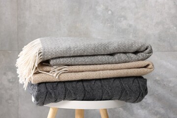 Folded woolen plaids on table near grey wall, closeup