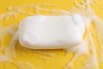 Soap bar with foam on yellow background, closeup