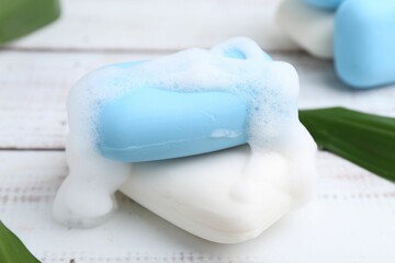 Soap bars with foam on white wooden table, closeup