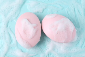 Soap bars with foam on light blue background, flat lay