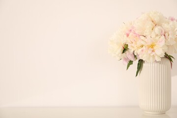 Bouquet of beautiful peonies on table near white wall. Space for text