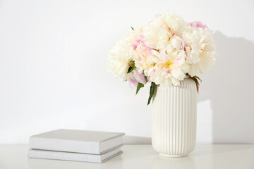 Bouquet of beautiful peonies and books on table near white wall. Space for text