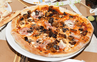 Delicious Italian pizza with mushrooms, ham, and cheese on a white plate