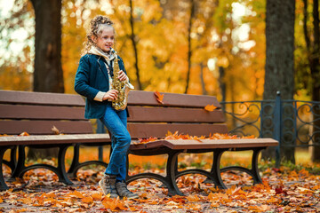 Young girl playing saxophone in autumn park.